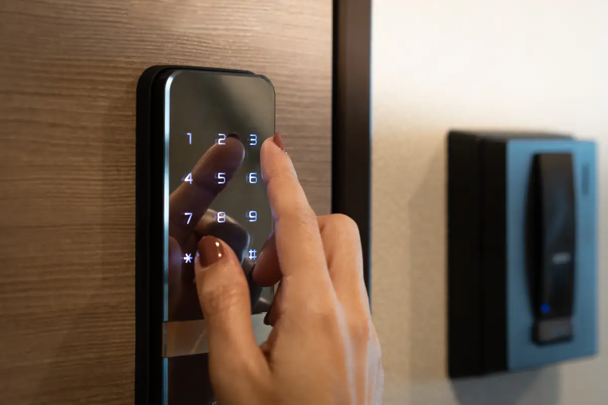 A person's hand is entering a code on a digital keypad lock installed on a wooden door. The illuminated number pad is being used for secure access.