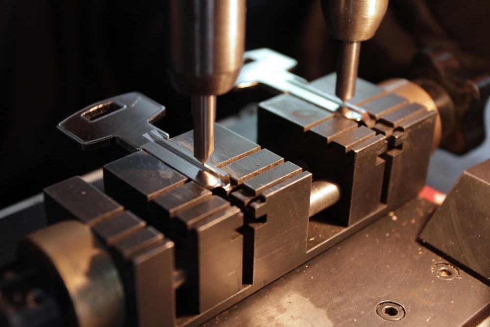 A close-up of a key being cut by a key duplicating machine in PA, with the key held in place by a metal vise as the cutting tool shapes its edge—showcasing expert locksmith services Delaware County residents trust.