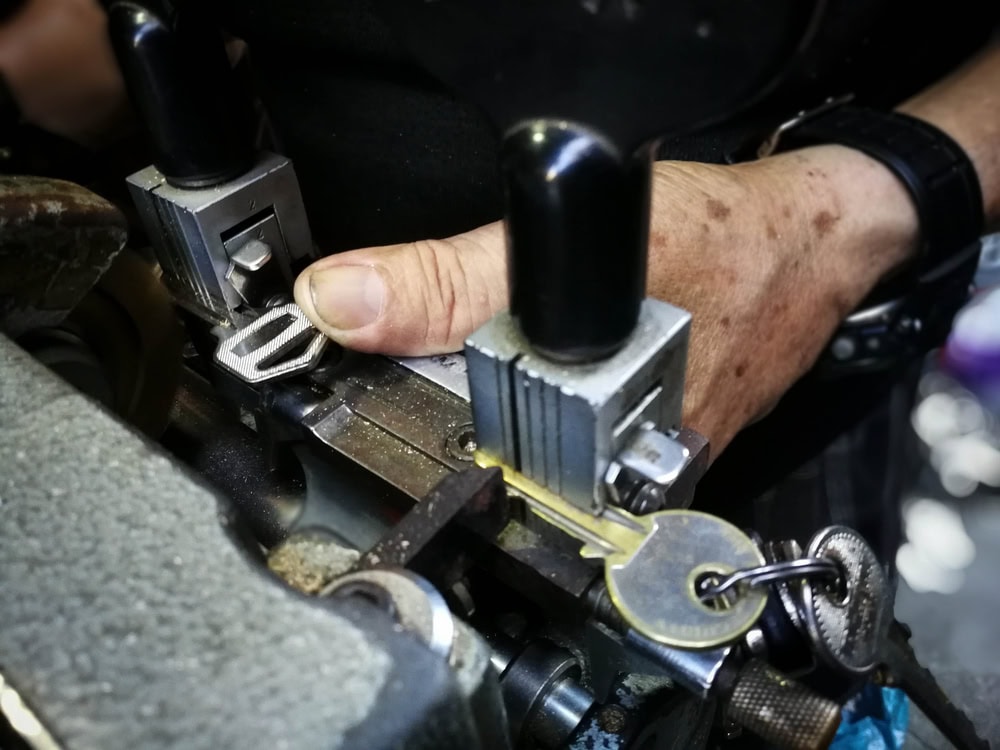 A close-up of a locksmith's hands operating a key cutting machine, with a key being duplicated and several keys on a key ring visible—showcasing expert Locksmith Services Delaware County, PA.