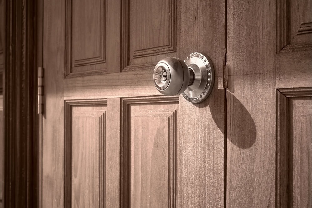 A close-up of a wooden door with a round metallic doorknob casting a shadow, highlighting the door’s panel design and texture—perfect for showcasing Locksmith Services Delaware County, PA.