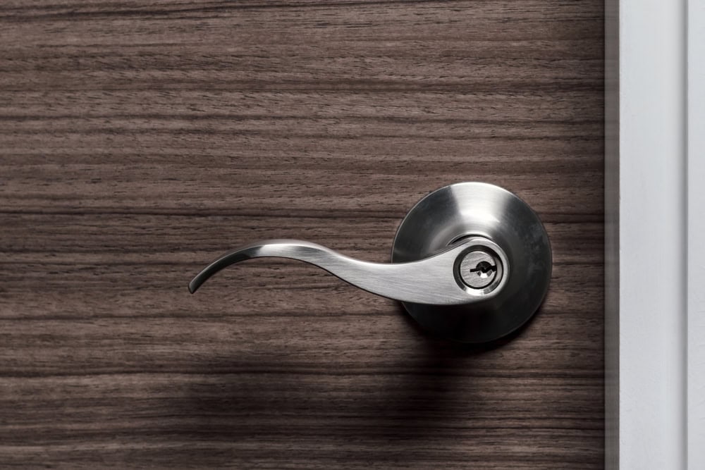 Close-up of a silver door handle with a keyhole on a wood-patterned door. The modern, sleek design stands out—ideal for homes in PA seeking Locksmith Services Delaware County can trust. The handle sits near the edge, bordered by a white frame.