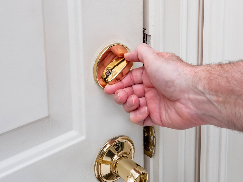 A close-up of a person’s hand locking a white door with a brass deadbolt latch, highlighting Locksmith Services Delaware County, PA.
