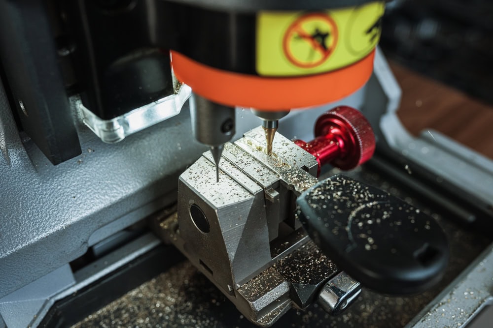 A close-up of a key-cutting machine in operation, with a key blank held in a clamp as the cutting drill shapes the key—metal shavings visible—demonstrates the precision offered by Locksmith Services Delaware County, PA.