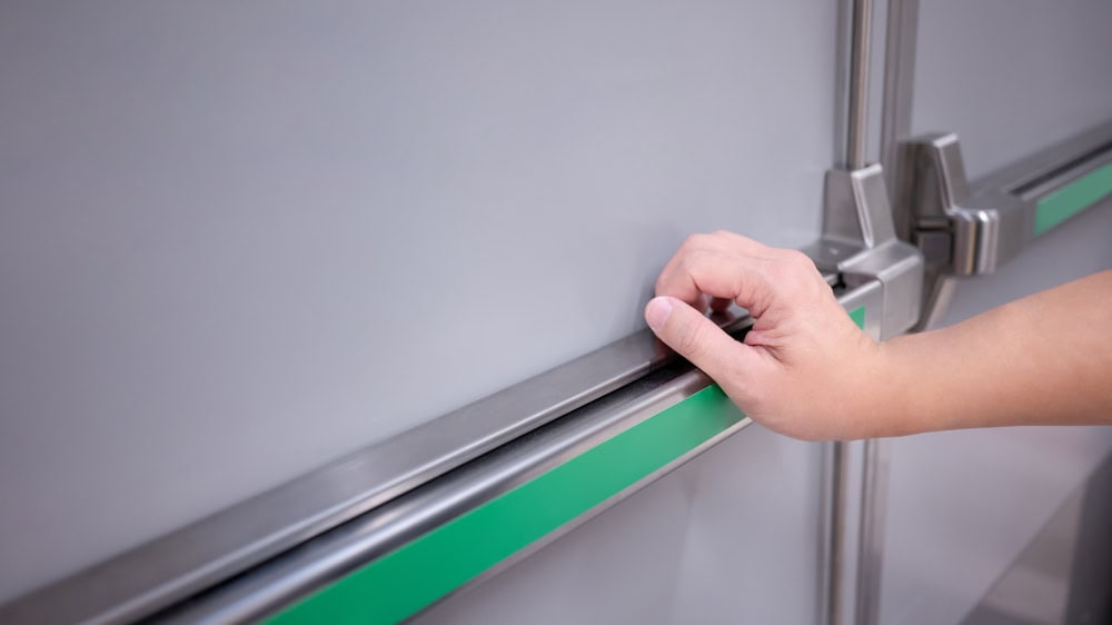 A person's hand grasping the metal handle of a sealed door with a green stripe, possibly an emergency exit or industrial refrigerator door in PA, highlighting the importance of Locksmith Services Delaware County.