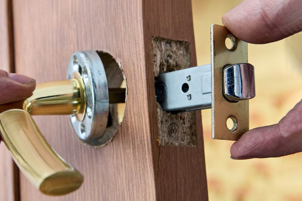 Close-up of hands installing a door handle and latch mechanism into a wooden door in PA. The gold-colored handle and metal plate are being carefully aligned—showcasing expert Locksmith Services Delaware County can trust.