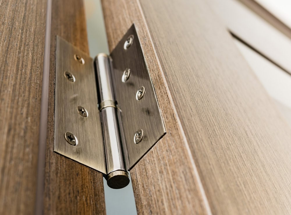 Close-up view of a shiny metal door hinge attached to a wooden door and frame, highlighting the hardware and wood texture—perfect for showcasing the quality work offered by Locksmith Services Delaware County, PA.