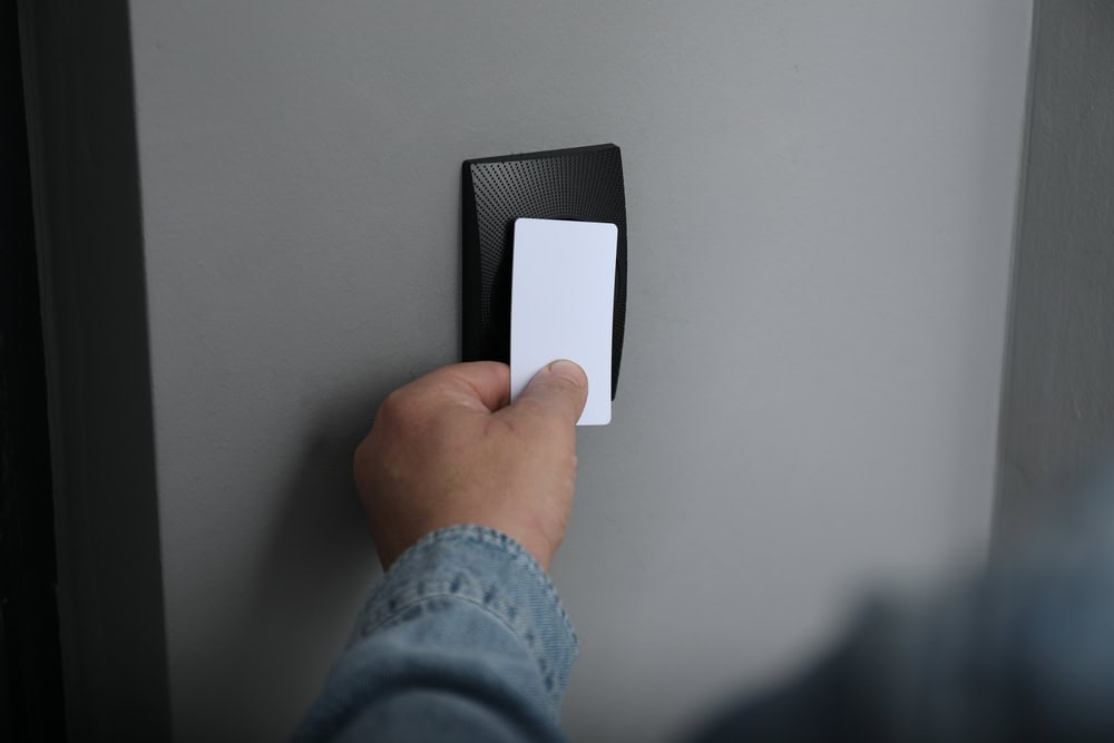 A person holds a white key card up to a black card reader mounted on a gray wall, demonstrating modern access solutions often used by Locksmith Services Delaware County, PA.