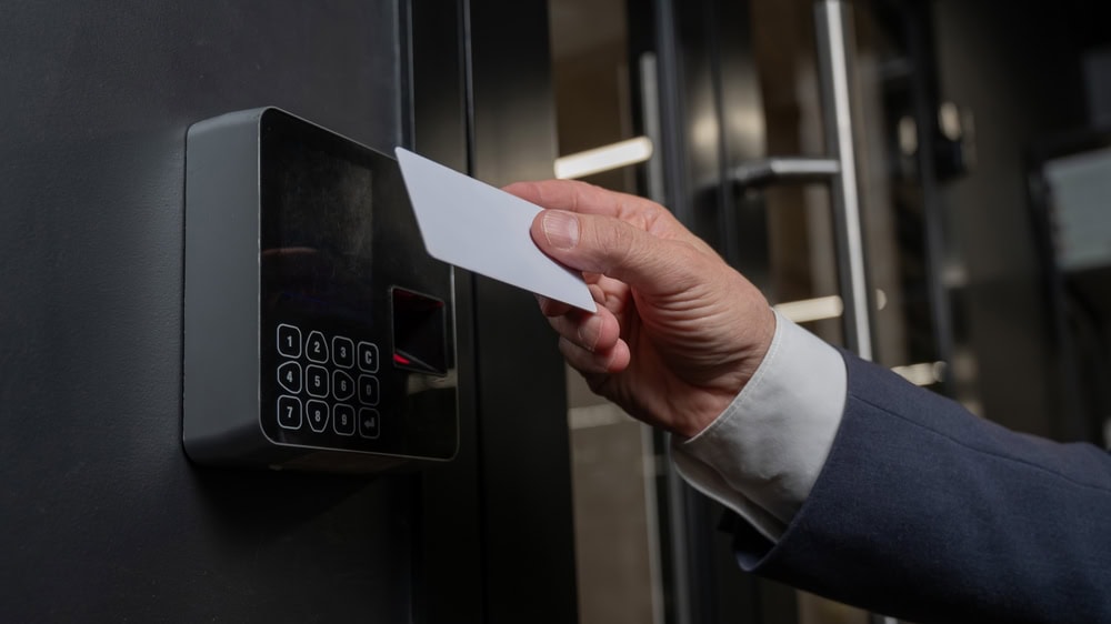 A person in a suit holds a white access card up to an electronic keypad reader, likely to unlock a secure door—demonstrating the advanced solutions offered by Locksmith Services Delaware County, PA.