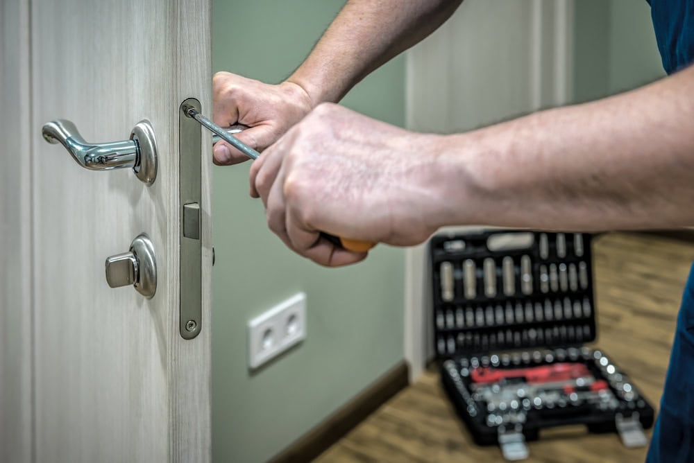 A person uses a screwdriver to fix or install a door lock, with a tool kit open on the floor nearby—perfect for those seeking Locksmith Services in Delaware County, PA.
