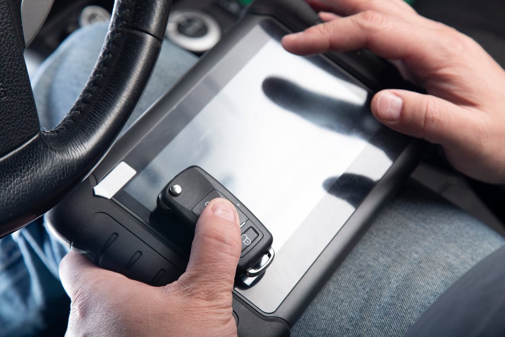 A person holds a car key fob against a diagnostic tablet inside a vehicle, possibly programming or testing the key—demonstrating expert Locksmith Services Delaware County, PA—with the steering wheel and dashboard visible in the background.