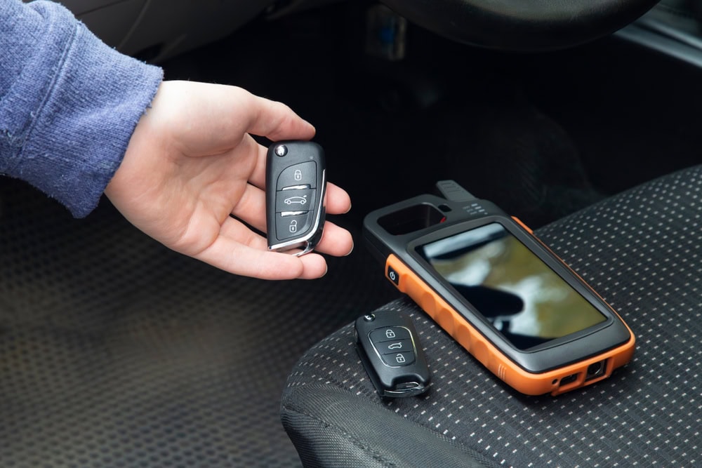 A hand holds a car key fob above a car seat in PA, where another key fob and an orange automotive diagnostic tool rest—perfect for those seeking Locksmith Services Delaware County.
