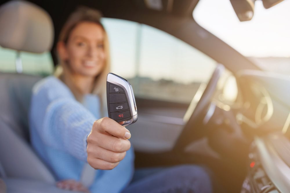 A person sitting in a car holds a car key fob toward the camera, smiling, showcasing the convenience of Locksmith Services Delaware County, PA. The focus is on the key, while the individual is slightly blurred in the background.
