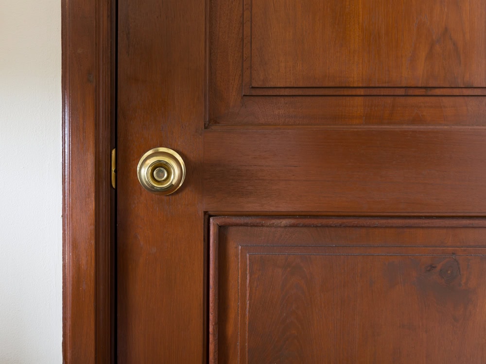 A close-up view of a wooden door with a brass doorknob, ideal for PA homes. The door has a rich brown finish and rectangular panels, with part of a white wall visible on the left—a perfect example for Locksmith Services Delaware County.