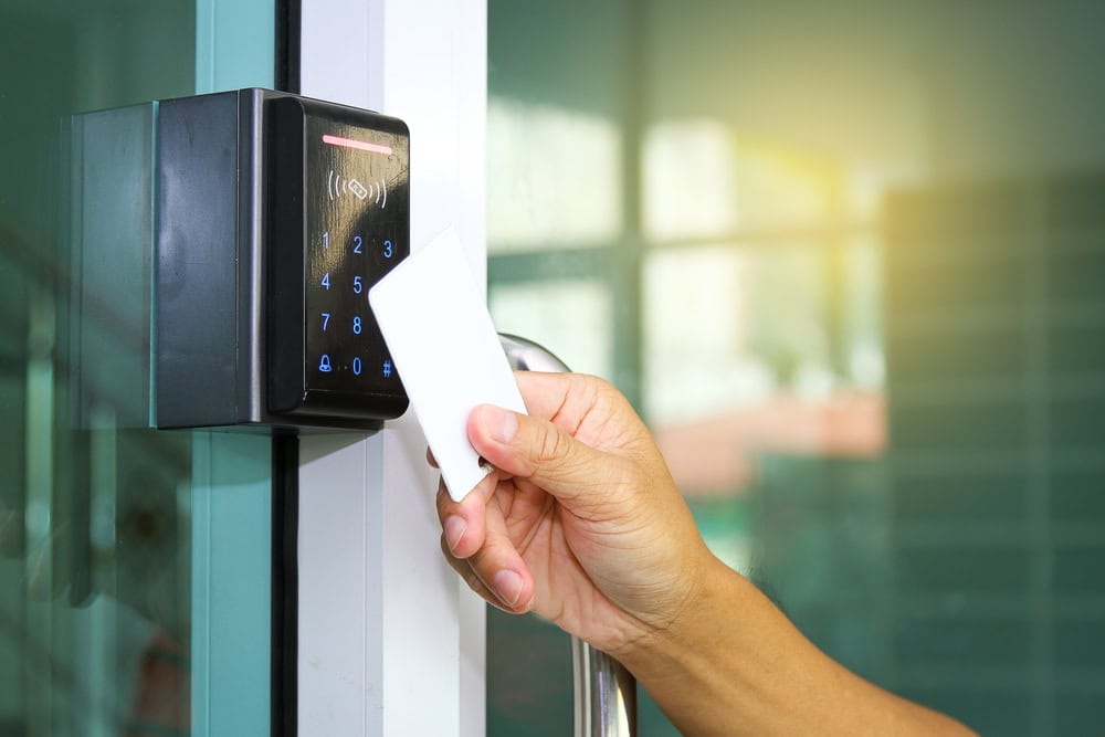 A person holds a white key card up to an electronic access control keypad, preparing to unlock a glass door—showcasing the modern security solutions provided by Locksmith Services Delaware County, PA.
