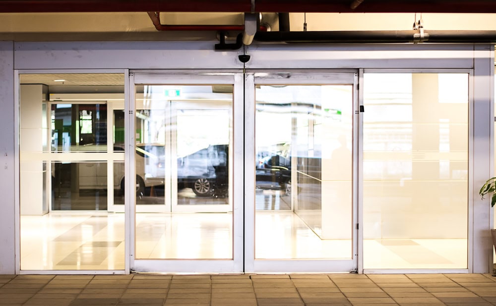 Automatic glass sliding doors at the entrance of a modern PA building, with reflections visible on the doors and a tiled floor in the foreground—secured with top-notch Locksmith Services Delaware County offers.