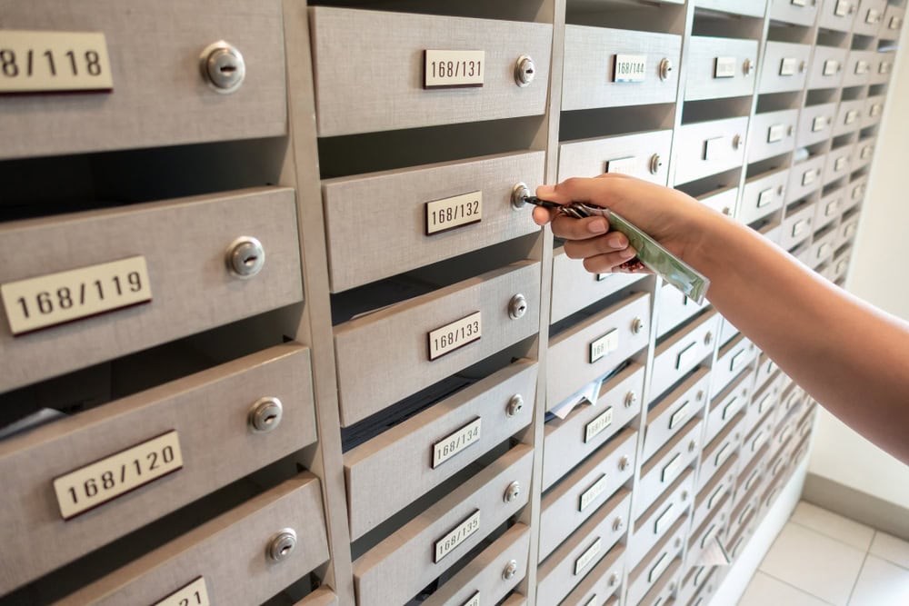 A person’s hand inserts a key into a mailbox lock in a wall of numbered mailboxes, each with a small slot and label, inside what appears to be an apartment or office building in PA—perfect for those seeking Locksmith Services Delaware County.