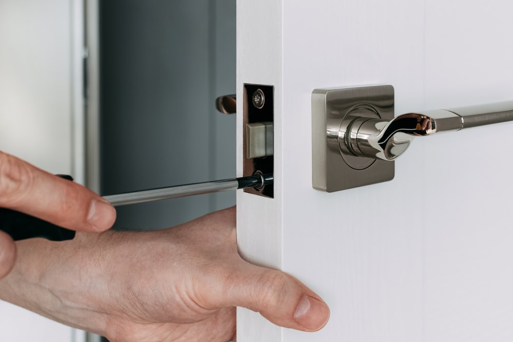 A close-up of a person’s hands using a screwdriver to install or adjust a silver door lock and handle on a white door, demonstrating professional Locksmith Services Delaware County, PA.