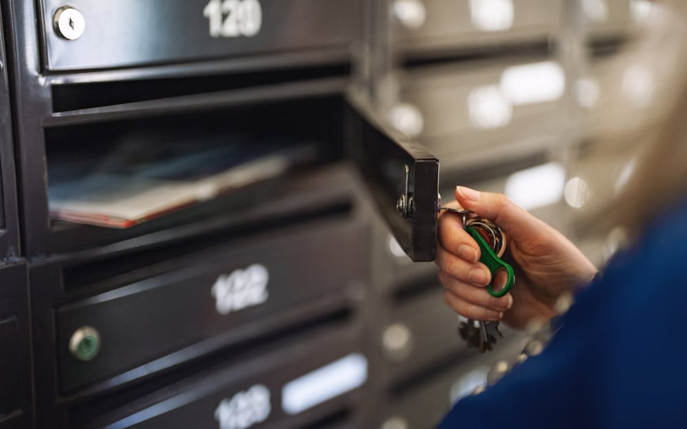 A person holds a set of keys and opens a black mailbox, revealing envelopes and mail inside. The numbered mailboxes hint at secure access—perfect for those seeking Locksmith Services in Delaware County, PA. Focus is on the hand, key, and open mailbox.