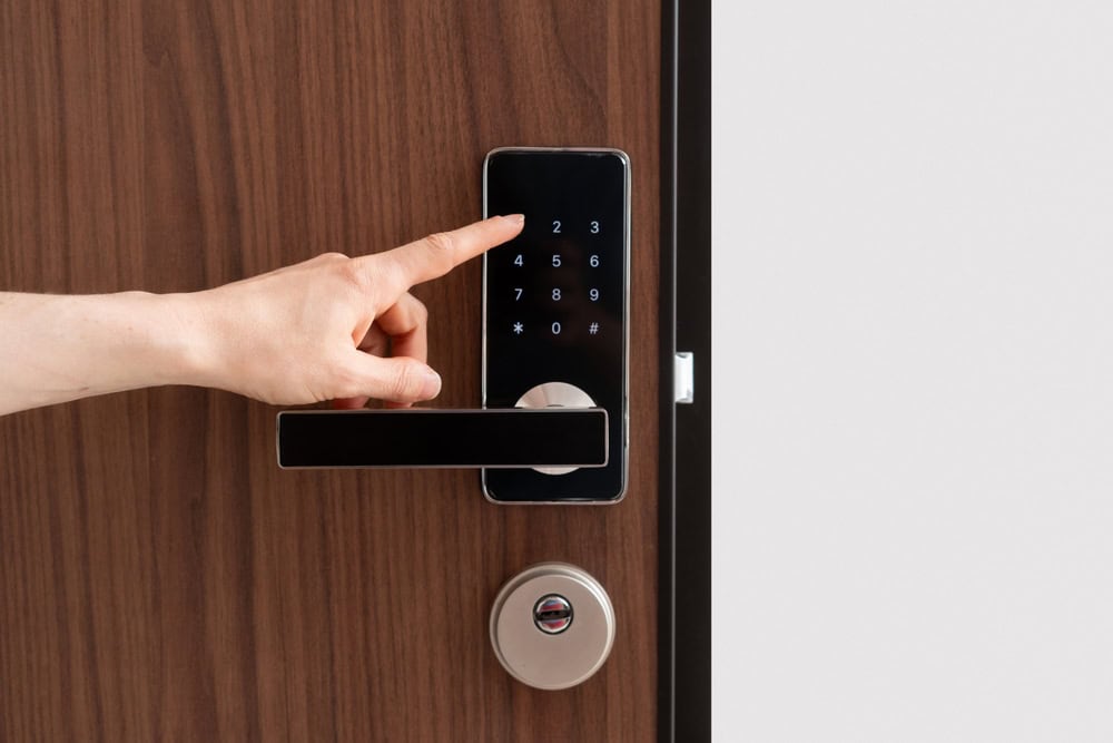 A person’s hand is pressing buttons on a digital keypad lock installed on a wooden door above a modern handle and a traditional keyhole lock, showcasing advanced security solutions by Locksmith Services Delaware County, PA.