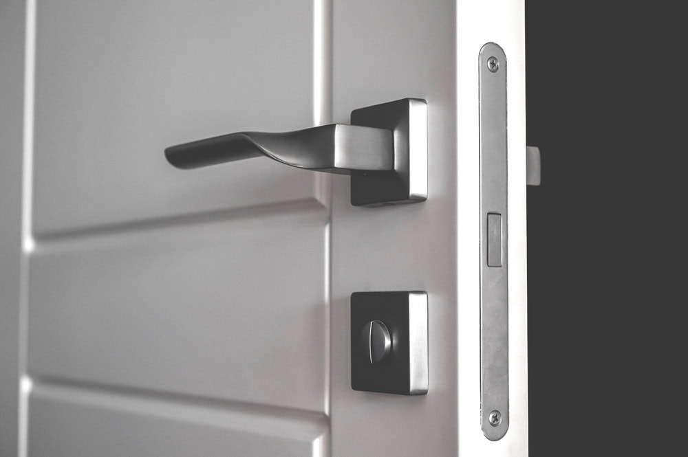 A close-up view of a modern, silver door handle and lock on a slightly open white interior door in PA, with a dark background visible through the opening—ideal for showcasing Locksmith Services Delaware County.